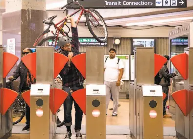  ?? Jessica Christian / The Chronicle ?? A commuter struggles to get himself and his bike through a prototype fare gate at the Richmond BART Station.