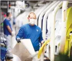  ?? (AP) ?? In this file photo, an employee
walks past vehicles in production with a face mask in the VW
plant in Wolfsburg, Germany.
Volkswagen is gradually launching the production at important plants after the corona lockdown.