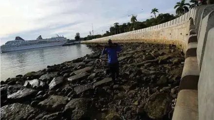  ?? (Foto Mikail ONG/BH) ?? Pekerja Majlis Bandaraya Pulau Pinang (MBPP) membersihk­an kawasan takungan air akibat air pasang besar di persiaran teres bawah (Lower Terrace) Tembok Laut yang dicemari sampah sarap di Jalan Tun Syed Sheh Barakbah, Padang Kota Lama, Georgetown, semalam.