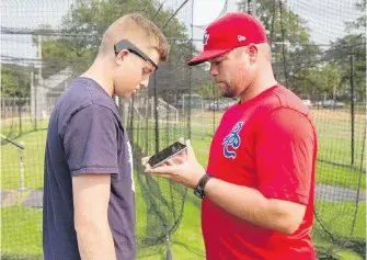  ??  ?? Victoria HarbourCat­s’ Cole Weiss, left, has his brain activity tested by University of Victoria student Anthony Pluta during batting practice.