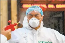  ?? AFP/Getty Images ?? AT A quarantine zone in Wuhan, a doctor is disinfecte­d by a colleague in February. At least 18 medical workers have died, some because of overwork and fatigue.