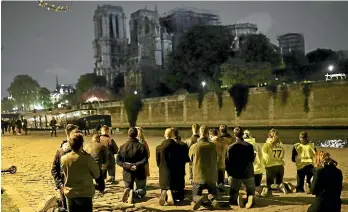  ?? AP ?? People pray on their knees by the Seine in front of the Notre Dame Cathedral in Paris. A frantic rescue effort saved the monument’s ‘‘most precious treasures,’’ including the relic revered as Jesus’ Crown of Thorns, officials said.