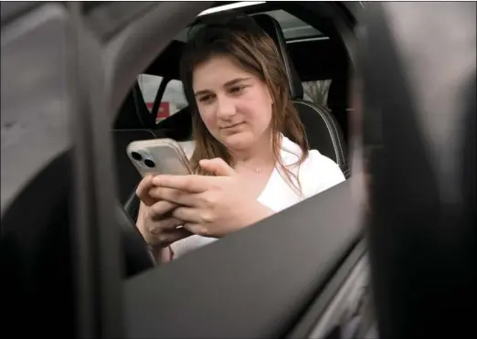  ?? AP Photo/Steven Senne ?? Alexis Bogan, whose speech was impaired by a brain tumor, uses an AI powered smartphone app to create a audible drink order at a Starbucks drive-thru on Monday, April 29, in Lincoln. The app converts her typed entries into a verbal message created using her original voice.