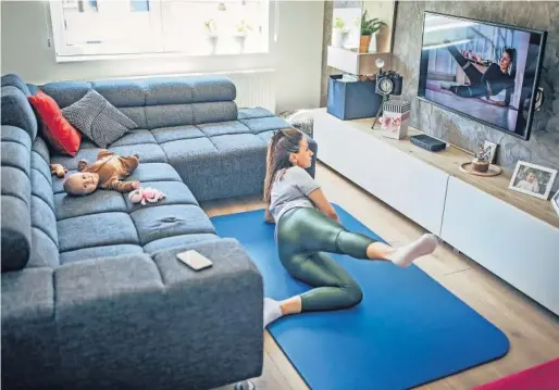  ?? SOUTH_AGENCY (GETTY IMAGES) ?? Una mujer hace ejercicio frente al televisor y su bebé mira a cámara desde el sofá.