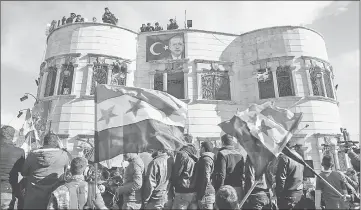  ??  ?? A banner bearing the Turkish flag and a picture of Erdogan is seen hanging from a building while Syrians wave rebel flags during a demonstrat­ion below in the rebel-held town of Azaz in northern Syria in support of a joint rebel and Turkish military...