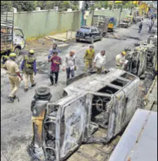  ??  ?? Police and residents walk past charred remains of vehicles vandalised by a mob over a social media post in Bengaluru on Wednesday.