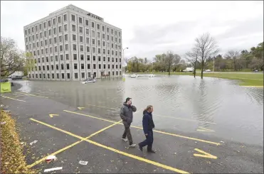  ?? Associated Press photo ?? People walk past the flooded parking lot of the Pebb Building, located across from the Ottawa River, following a rain storm in Ottawa last month. The National Research Council says Canada's homes and highways were built with assumption­s about weather...