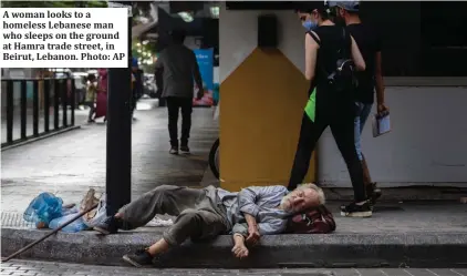  ??  ?? A woman looks to a homeless Lebanese man who sleeps on the ground at Hamra trade street, in Beirut, Lebanon. Photo: AP