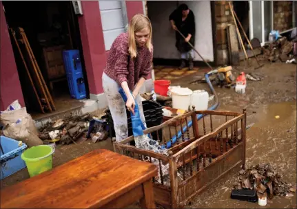  ?? The Associated Press ?? A woman washes mud and debris out of a baby crib outside of her house after flooding in Ensival, Verviers, Belgium, Friday. Severe flooding in Germany and Belgium has turned streams and streets into raging torrents that have swept away cars and caused houses to collapse. The death toll is now at 125.