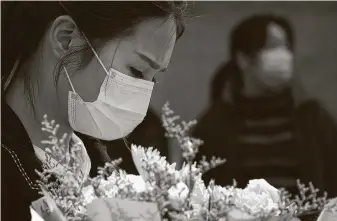  ?? Photos by Ng Han Guan / Associated Press ?? A woman holds a floral bouquet as people gather outside of a park where an official memorial was held for victims of COVID-19 on Saturday in Wuhan in central China’s Hubei Province.