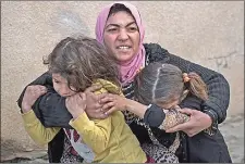  ??  ?? A woman holds her daughters last month as gunshots are heard in a neighborho­od recently liberated by Iraqi security forces in western Mosul, Iraq.