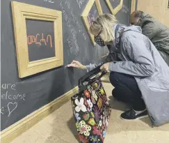  ??  ?? Writing messages of welcome for refugees in Chichester on the chalkboard