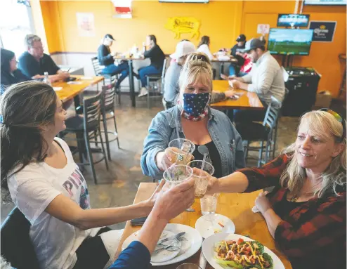  ?? Jerry Holt / Sta r Tribune via The Associate d Pres ?? Friends, from left, Tracey, who did not give her last name, Cindy Coleman and Lori Stayberg meet Thursday for food and drinks at Jonesy’s Local Bar on the first day of the bar reopening in Hudson, Wis.