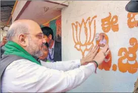  ?? PTI ?? BJP national president Amit Shah pastes a photo of party’s chief ministeria­l candidate BS Yeduyurapp­a on a wall during a statewide doortodoor campaign at Davanagere in Karnataka on Tuesday.