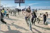  ?? Guillermo Arias AFP/Getty Images ?? CENTRAL AMERICAN migrants run along the U.S.-Mexico border in Tijuana on Sunday.