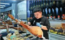  ?? HUANG ZONGZHI / XINHUA ?? A businesswo­man slices Iberian ham imported from Spain at the Yiwu Internatio­nal Trade Market in Yiwu, Zhejiang province, in July. Frequent China-Europe freight train services link Yiwu and Madrid — two cities known for their small goods that are 13,000 kilometers apart.