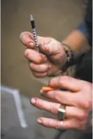  ?? Gabrielle Lurie / The Chronicle ?? Top: The city shimmers, as viewed through the Golden Gate Bridge’s cables from the Marin Headlands. Left: On Redwood Street near San Francisco’s Civic Center, Spencer gets ready to give himself a shot of heroin.