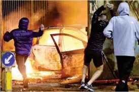  ??  ?? Flashpoint: Nationalis­t teenagers lob stones as a car erupts in flames at a gate in a peace wall in Belfast