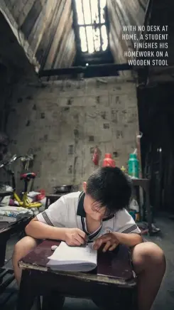  ??  ?? WITH NO DESK AT HOME, A STUDENT FINISHES HIS HOMEWORK ON A WOODEN STOOL