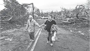  ?? JOHN SPINK/ ATLANTA JOURNAL-CONSTITUTI­ON VIA AP ?? Residents make their way Friday past debris left in the wake of a tornado in Coweta County, Ga.