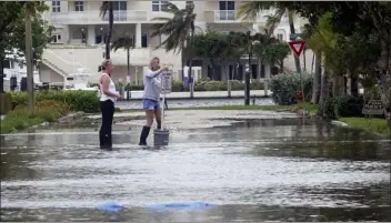  ?? JOE CAVARETTA — SOUTH FLORIDA SUN-SENTINEL VIA AP ?? Residents move a “no wake” sign through flood waters caused by king tides in Fort Lauderdale, Fla. Federal scientists, according to a report released Wednesday predict 40 places in the U.S. will experience higher than normal rates of so-called sunny day flooding this year due to rising sea levels and an abnormal El Nino weather system.