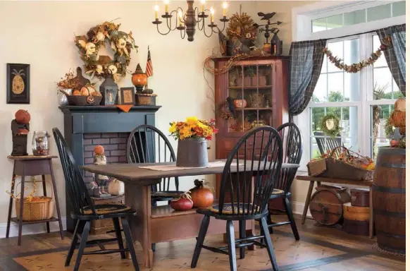  ??  ?? Below: Open to the kitchen, the dining room is Julie’s favorite space in the house. Black elements, such as a faux fireplace, painted chairs and dark curtains, are toned down by a painted floorcloth and furnishing­s finished in ruddy tones. The bench under the window and the firkin on the table were passed down to Julie from her great-grandmothe­r.