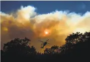  ?? Noah Berger / Associated Press ?? Smoke billows Monday from the Camp Fire as a firefighti­ng copter flies near Pulga (Butte County).