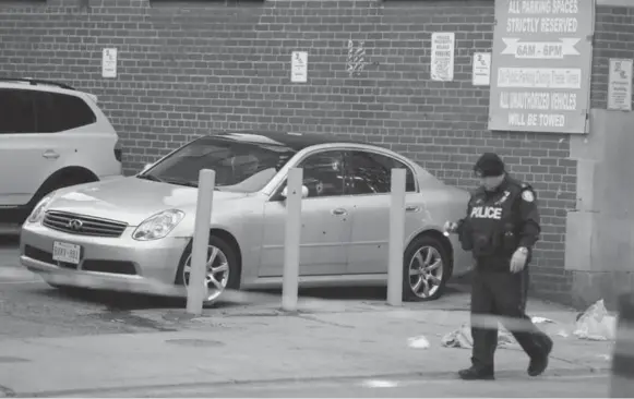  ?? STEVE RUSSELL/TORONTO STAR ?? A Toronto police officer walks by a car riddled with bullet holes near King and Peter Sts. after an apparent drive-by shooting. A man inside the vehicle was killed. A woman escaped unharmed.