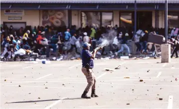  ??  ?? A policeman disperses looters in Johannesbu­rg on Tuesday