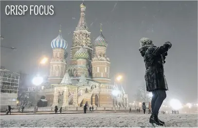  ?? Picture: AFP ?? A woman takes pictures in Red Square in front of St Basil’s Cathedral as it snows in Moscow on Tuesday.