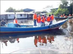  ??  ?? Dr Murni uses a net to collect floating rubbish in a river while others look on during the programme.