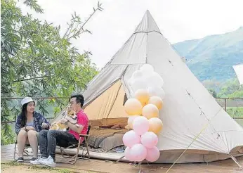  ?? MATTHEW CHENG/ AP ?? A young couple with their dog spend time outside an Indian-style tent at We Camp, a glamping site located in Yuen Long, Hong Kong, in August 2021.