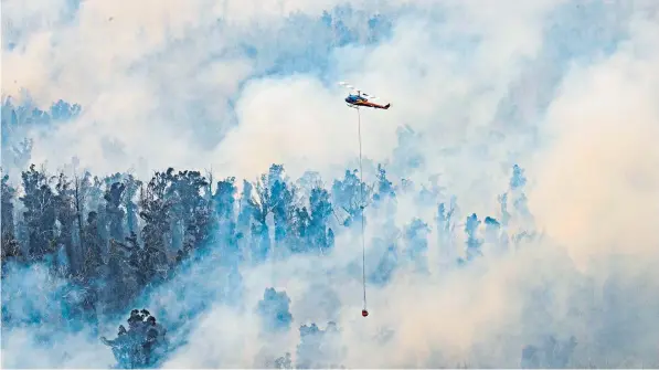  ??  ?? A helicopter dumps water on a fire in Victoria’s East Gippsland, a region popular with holidaymak­ers
