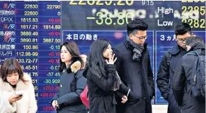  ??  ?? Pedestrian­s pass an electronic stock indicator in Tokyo last week. The Japanese stock market could benefit from a stronger dollar on the back of higher interest rates next year