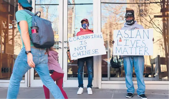  ?? MICHAEL M. SANTIAGO/GETTY ?? Cameron Hunt and his father, Calvin Hunt, hold signs of support as they stand Tuesday near the spot where an Asian American woman was attacked Monday in New York City. The NYPD is calling the attack a hate crime.