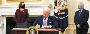  ?? The Associated Press ?? Q President Joe Biden signs executive orders after speaking about the coronaviru­s, accompanie­d by Vice President Kamala Harris, left, and Dr. Anthony Fauci, director of the National Institute of Allergy and Infectious Diseases, right, in the State Dining Room of the White House Thursday in Washington.