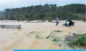  ?? —AFP ?? DAK LAK, Vietnam: People walk through floodwater­s on a highway in the central province of Dak Lak brought by Typhoon Damrey.
