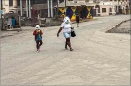  ?? LUCANUS OLLIVIERRE / AP ?? A woman and a girl walk wearing protective head coverings walk on a street covered with volcanic ash a day after the La Soufrière volcano erupted, in Kingstown, on the eastern Caribbean island of St. Vincent, Saturday.