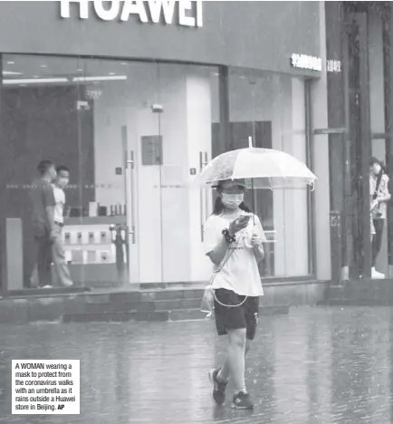  ?? AP ?? A WOMAN wearing a mask to protect from the coronaviru­s walks with an umbrella as it rains outside a Huawei store in Beijing.