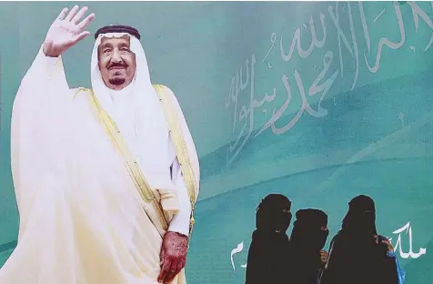  ?? REUTERS ?? Women walk past a poster of Saudi Arabia’s King Salman bin Abdulaziz Al Saud during the Janadriyah Cultural Festival in Riyadh on Friday.