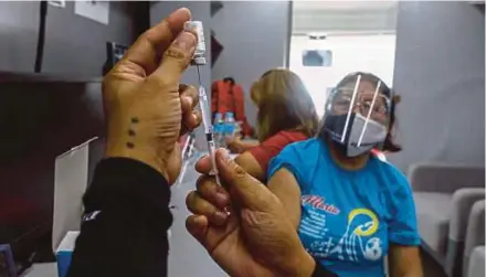  ?? EPA PIC ?? A health worker preparing the Sinovac Covid-19 vaccine for a woman in a bus converted into a vaccinatio­n hub in Quezon City, Metro Manila, recently.