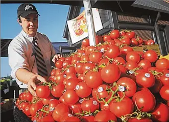  ?? MARSHALL GORBY / STAFF ?? Nick Budding, assistant produce manager for Dorothy Lane Market, places tomatoes on an outdoor display Thursday. Weekend forecasts call for much warmer, muggier conditions.