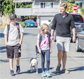  ?? DARREN STONE, TIMES COLONIST ?? Dean Murdock walks on Birchwood Street near Blair Avenue with children Caelum, 11, and Avery, 9, and dog Bella. There are no sidewalks in the area so Murdock has started a group called Better Mobility Saanich that’s aimed at getting safer infrastruc­ture for those walking and cycling in Saanich.