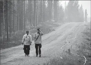  ?? AP/ RASHAH McCHESNEY ?? Two firefighte­rs walk on a road near a forest ravaged by the Card Street fi re in Sterling, Alaska, in
this fi le photo.