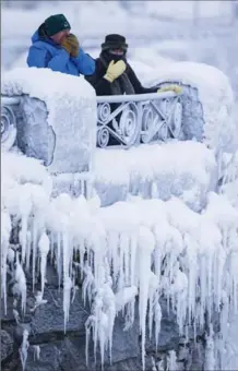  ?? AARON LYNETT, THE CANADIAN PRESS ?? Visitors try to keep warm at the brink of the Horseshoe Falls in Niagara Falls as freezing temperatur­es and mist from the falls continues to build on dramatic ice sculptures around the falls.