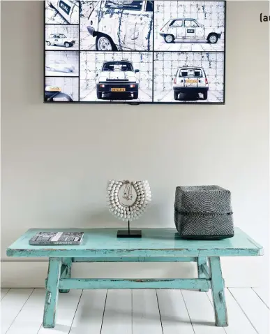  ??  ?? Table en bois chinée aux puces. Dessus, un des nombreux colliers africains que Rick collection­ne. L’écran de télévision au mur affiche en fond d’écran une photo de la vieille Renault 5 familiale.