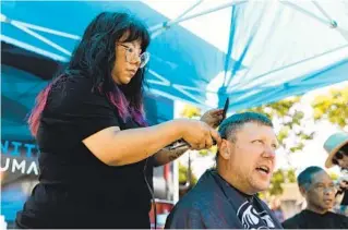  ?? KRISTIAN CARREON FOR THE U-T ?? John Stinson gets a haircut from barber Jessica Arenas during a homeless resource fair in the parking lot of Carlsbad City Library Learning Center on Friday.