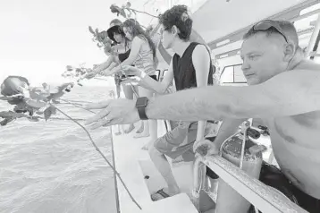  ??  ?? Will Payne, right, and three generation­s of his family throw flowers into the sea after a memorial plaque for Payne's parents, Buel and Linda Payne, was installed at the Neptune Memorial Reef near Miami Beach.