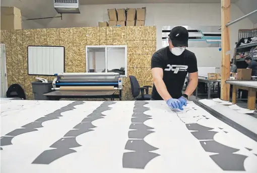  ?? Helen H. Richardson, The Denver Post ?? Andrew Martinez, director of operations of Xtreme Pro Apparel in Broomfield, lines up fabric cutouts on a table to put them through an oil drum heat press that transfers the ink from the paper onto the fabric that will become face masks.