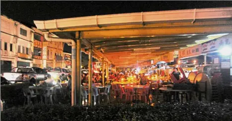  ??  ?? Making do: Patrons dining by candle and portable lighting at eateries along Jalan Gambir in Kuching. — Bernama